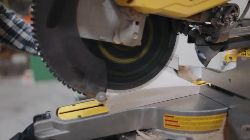 Slow motion close-up of a woodworker using a chop saw to precisely cut a wooden board in a workshop