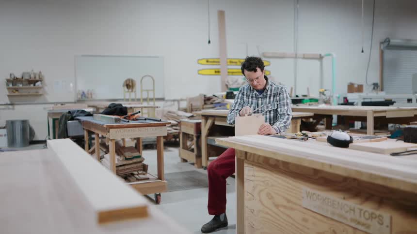 A skilled carpenter meticulously saws a dovetail joint by hand at a workbench in his spacious woodshop