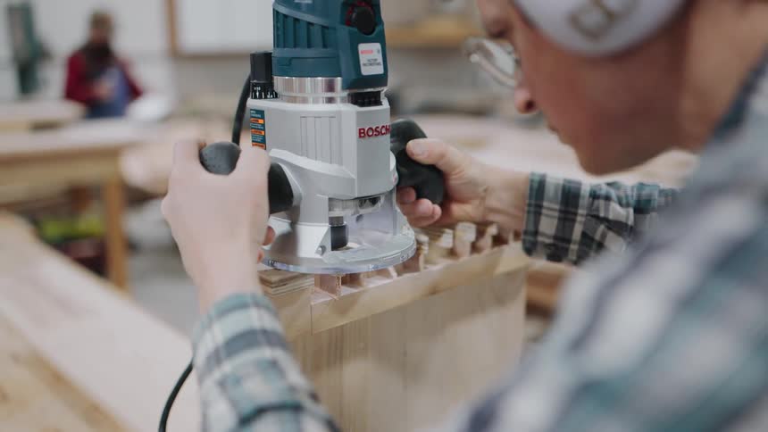 A skilled woodworker in a workshop meticulously cuts dovetail joints with a power router in slow motion