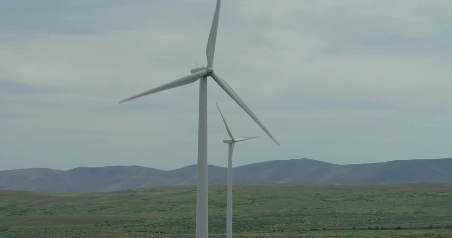 Aerial view of multiple large wind turbines spinning and generating clean energy on a vast green landscape under a cloudy sky