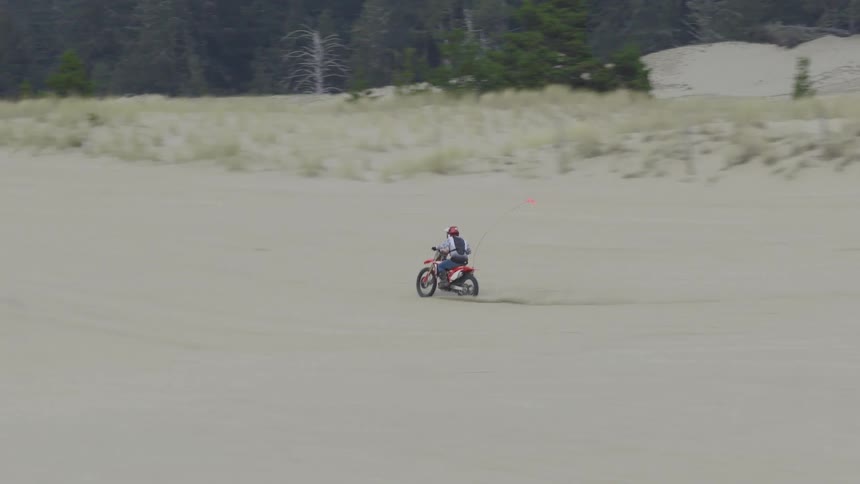 A skilled dirt bike rider performs a wheelie while speeding across a vast sand dune in slow motion