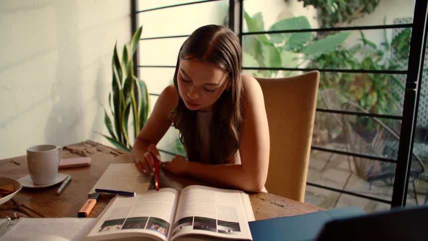 Happy female student diligently studying at her desk, pausing to daydream and smile