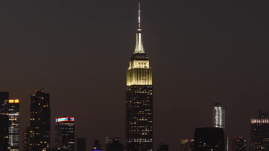 A slow zoom out reveals the Empire State Building standing tall and illuminated against the vast New York City skyline at night
