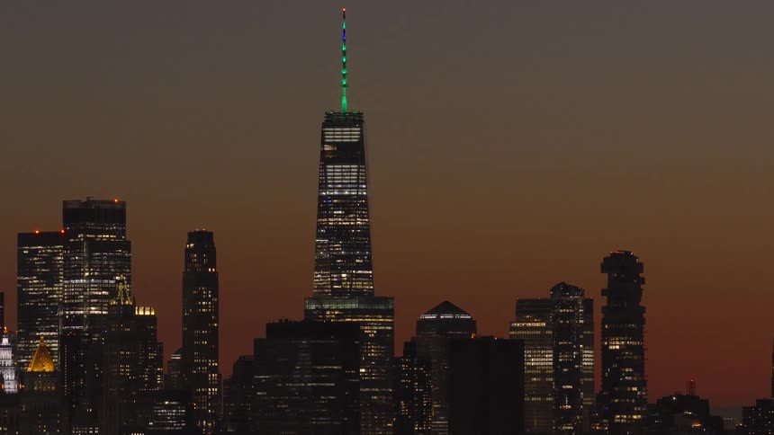 The iconic One World Trade Center stands tall amongst the illuminated Lower Manhattan skyline against a beautiful dusk sky