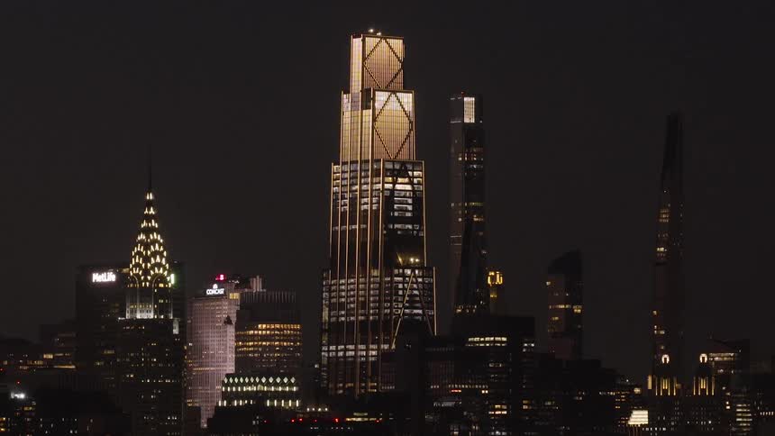 A slow zoom-out shot captures the brightly illuminated iconic skyscrapers of the Midtown Manhattan skyline against the dark night sky