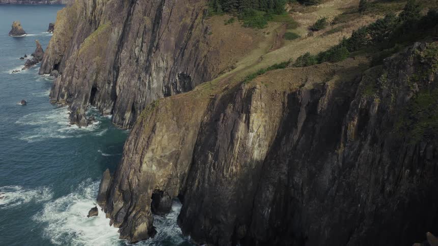 A stunning aerial shot pulls back to reveal a dramatic, rugged coastline with steep cliffs and sea caves carved by the powerful ocean waves