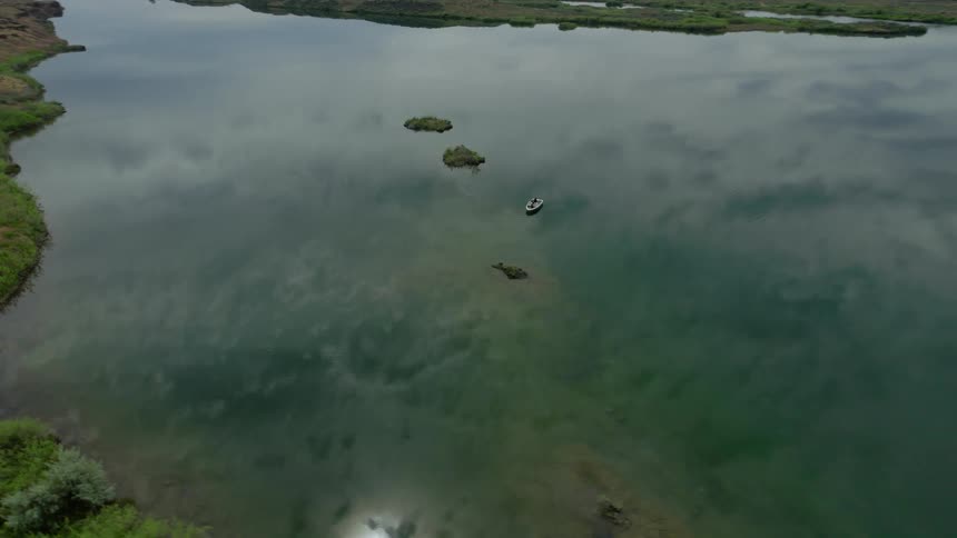 A stunning aerial view pulls back from a lone boat on a placid lake, perfectly reflecting the overcast sky in a vast, remote landscape