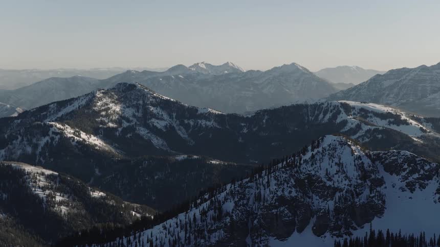 An expansive and serene landscape of snow-dusted mountains and pine forests under a clear winter sky