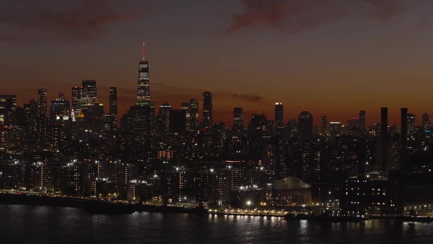 An iconic view of the Lower Manhattan skyline and One World Trade Center beautifully illuminated against a colorful twilight sky