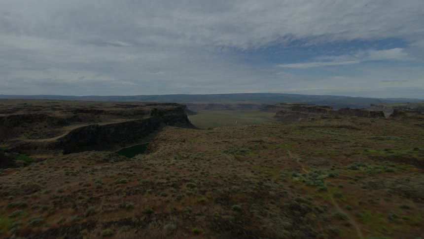 A sweeping aerial view flies over a vast, rugged landscape before revealing a tranquil lake nestled within a dramatic canyon