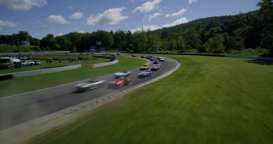 A thrilling aerial shot follows a pack of colorful vintage sports cars racing around a winding track on a sunny day