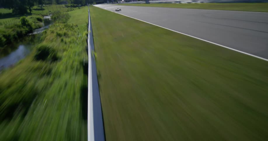 Thrilling aerial shot follows a Formula race car at high speed down the main straight of a scenic racetrack