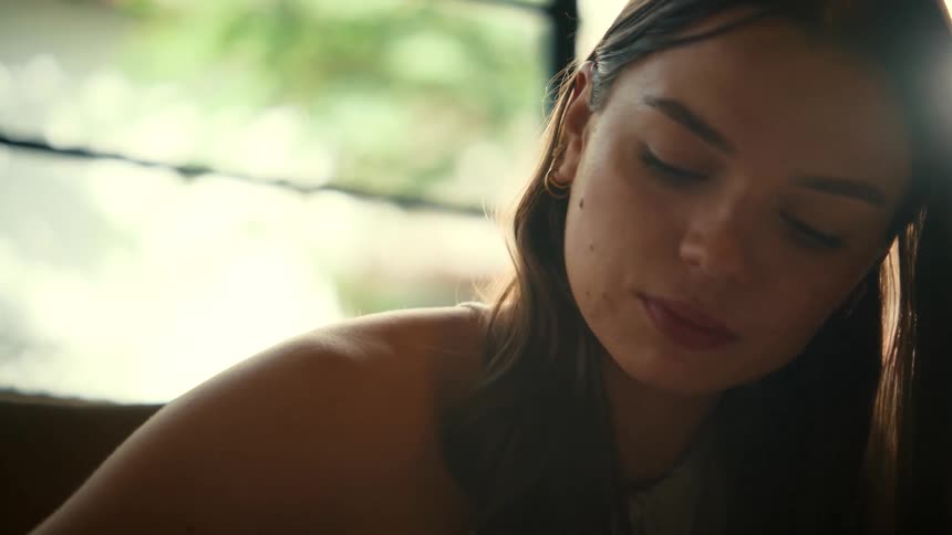 Close-up of a thoughtful young woman concentrating as she writes in a notebook in a warmly lit room