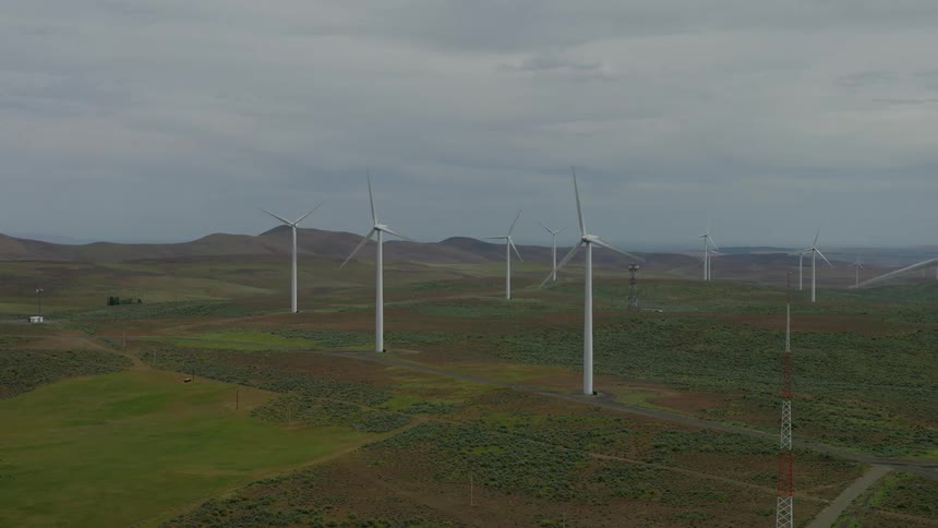Aerial shot flying over a vast wind farm with turbines generating clean energy across rolling green and brown hills