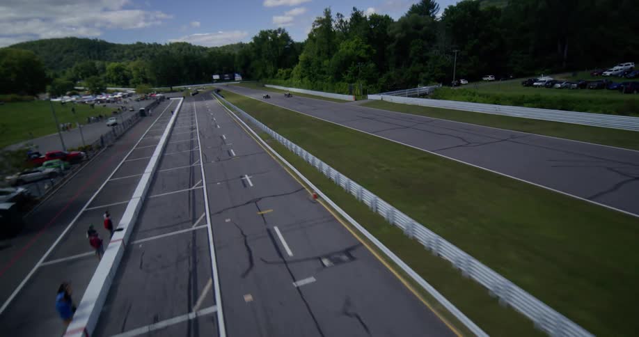 Dynamic aerial view follows two vintage race cars speeding down the main straight at Lime Rock Park on a sunny day