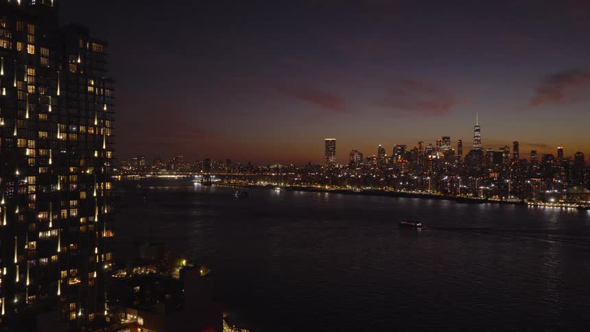 A stunning aerial view pulls back from a modern high-rise to reveal the iconic New York City skyline beautifully illuminated across the river at twilight