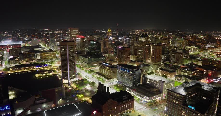 A stunning aerial view flies over Baltimore's Inner Harbor, showcasing the beautifully illuminated downtown city skyline at night