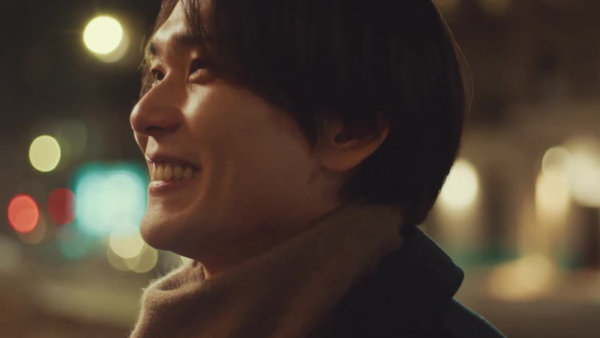 A young Asian man's face lights up with joy as his girlfriend surprises him with an emotional hug on a city street at night