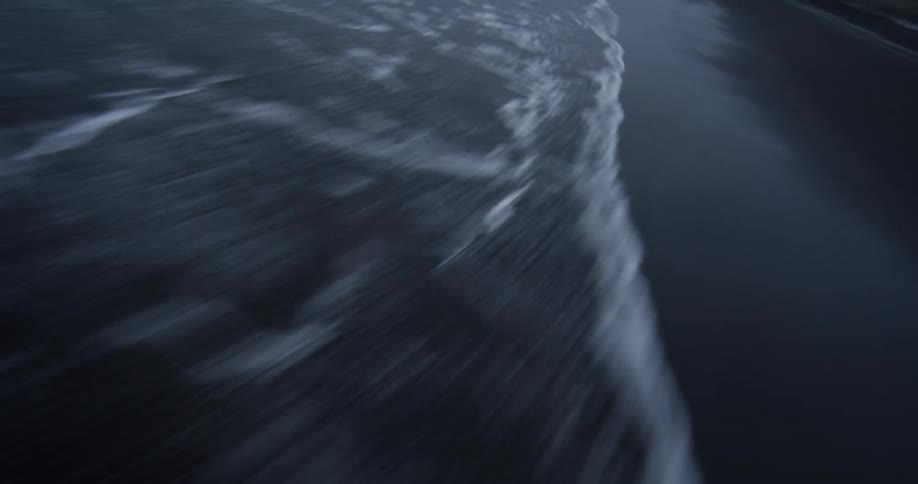 A dramatic, high-speed, low-angle shot captures the abstract motion blur of foamy ocean waves receding from a dark shoreline