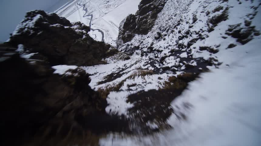An exhilarating aerial point-of-view flight swooping down through a snowy canyon over a rushing river