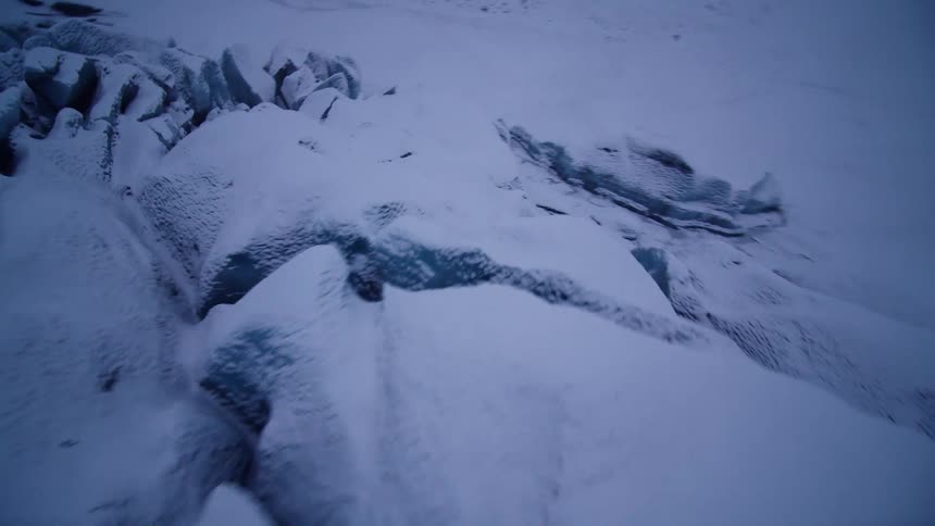 A fast-paced first-person-view aerial flight over the deep crevasses of a vast, snow-covered glacier in a cold, desolate landscape