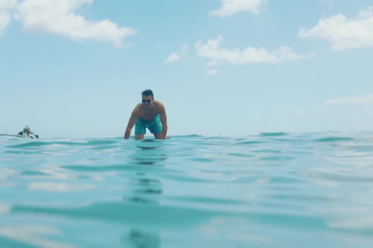 A surfer paddling on his knees gets knocked off his surfboard by a wave in the blue ocean