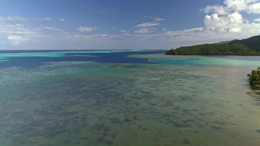 An aerial drone shot gracefully glides over a serene tropical bay, revealing a vibrant coral reef beneath the turquoise water