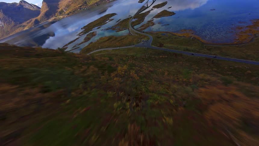 A breathtaking first-person-view aerial swoops down a rugged Norwegian mountainside to reveal a stunning fjord landscape with a scenic coastal road and bridge