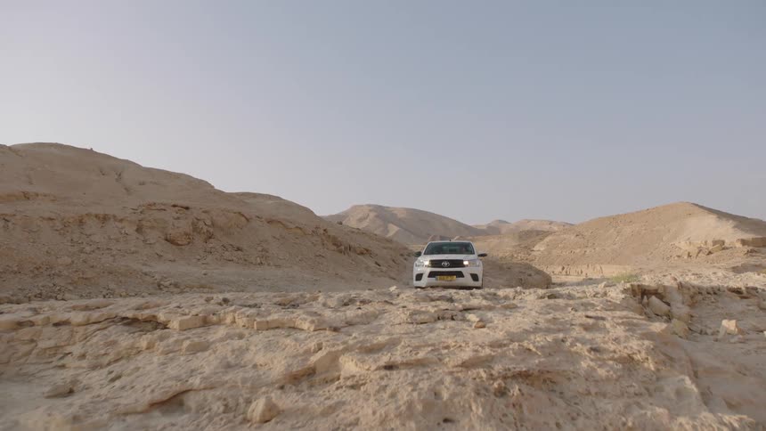 A white pickup truck navigates a rugged off-road trail through a dusty desert canyon
