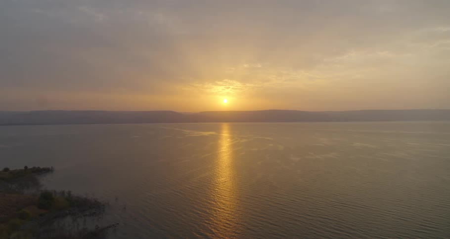 A serene golden sunset reflects over a tranquil lake with distant mountains on the horizon