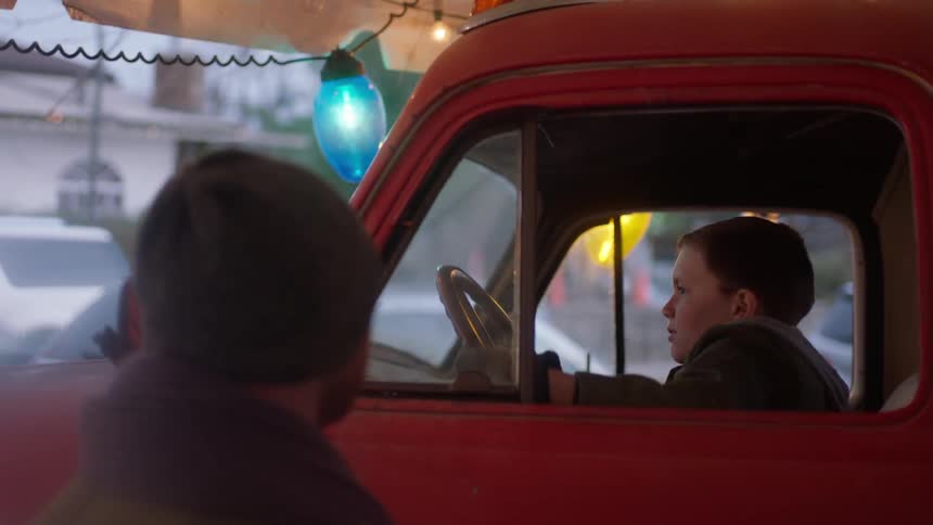 A man watches a kid pretends to drive a red truck