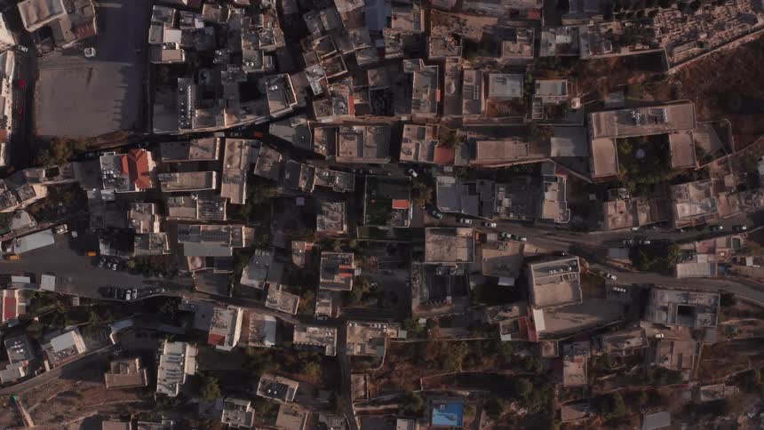 A static top-down aerial view of a densely populated ancient town with flat-roofed buildings and narrow streets at sunrise