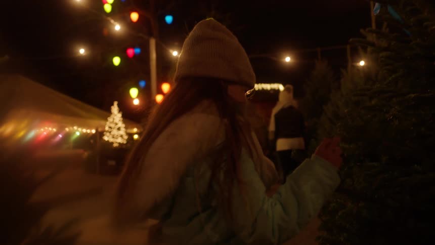 A girl looking and touching a christmas tree outside