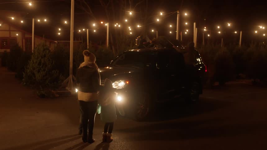 A woman and child watch on as a man ties a tree to a vehicle