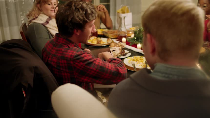 A man opens a gift while sitting at a dining room table with friends