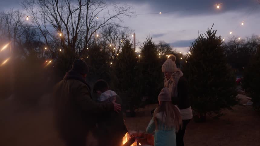 A group of people outside by a fire and surrounded by christmas trees