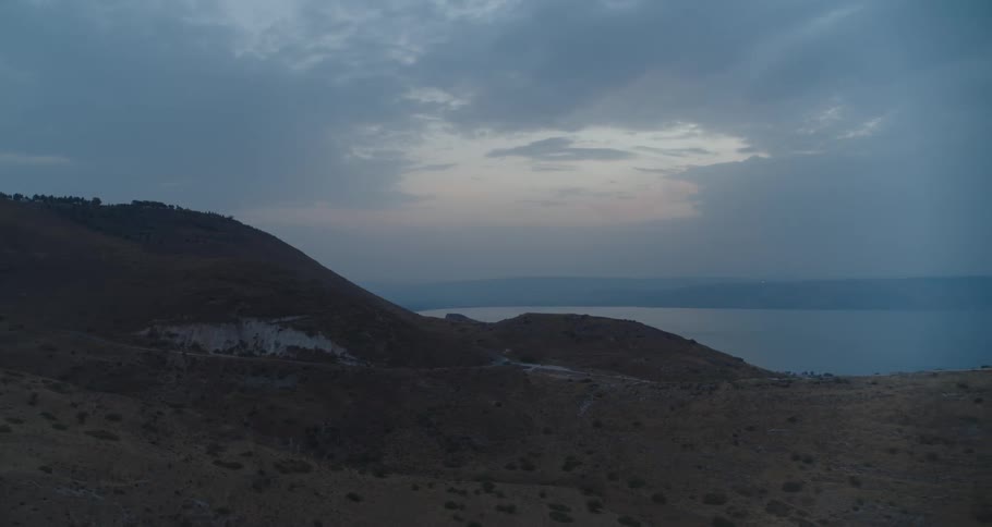 Gloomy hillsides overlook a tranquil lake under a vast, cloudy sky at dusk