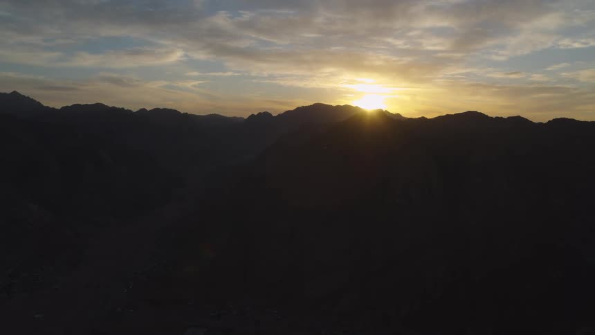 A static aerial view captures the sun rising over a vast, silhouetted mountain range at dawn