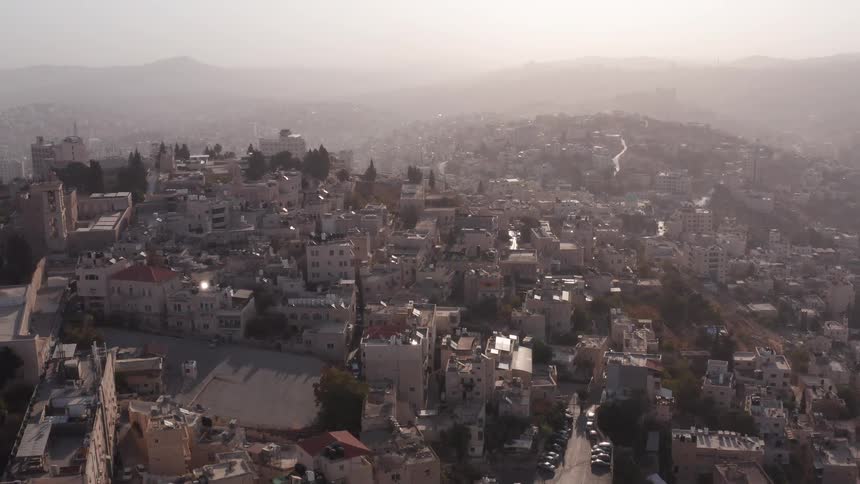 A slow aerial pullback reveals a sprawling, ancient city built into the hills, bathed in the hazy light of dawn