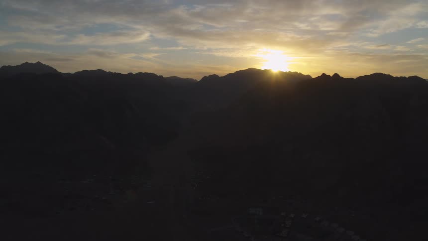 An aerial view captures the majestic sunrise over a silhouetted mountain range and a vast desert valley