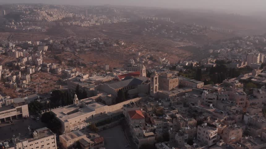 A hazy morning aerial view reveals the historic city of Bethlehem, with the Church of the Nativity at its center