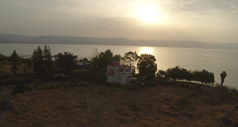 A slow aerial view pulls back from the Greek Orthodox Church of the Twelve Apostles on the shore of the Sea of Galilee at sunrise