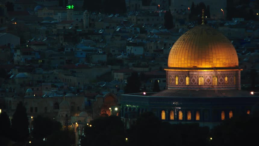 An establishing shot of the illuminated golden Dome of the Rock at night with the Old City of Jerusalem in the background