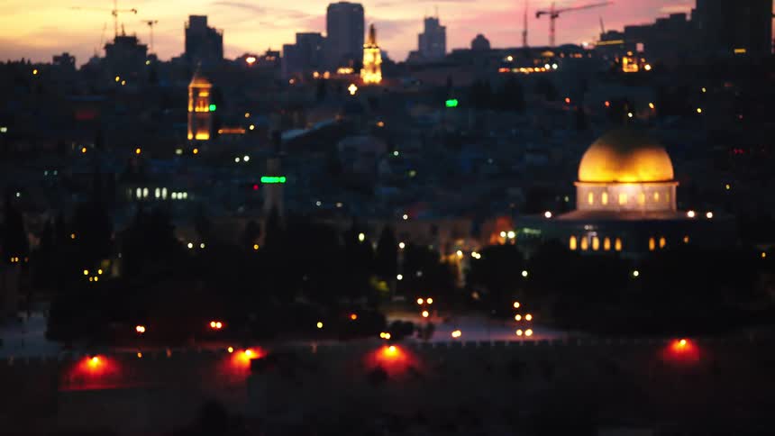 A beautiful pull focus shot reveals the illuminated Dome of the Rock and the Jerusalem cityscape at dusk