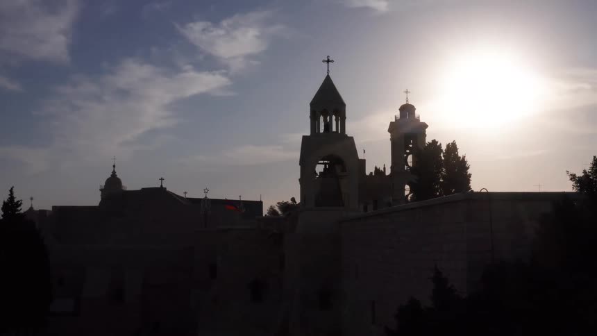 A slow aerial zoom reveals the silhouetted bell towers of the ancient Church of the Nativity in Bethlehem against the setting sun