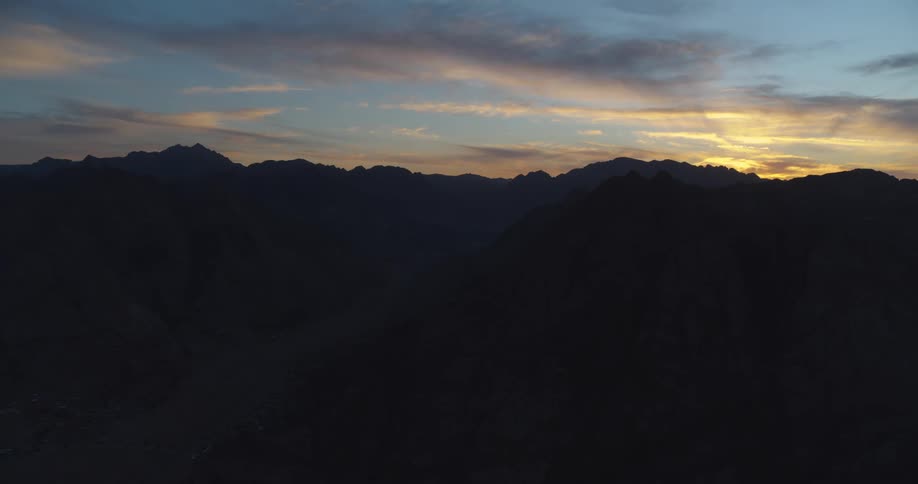 An aerial view of a majestic mountain range silhouetted against a beautiful twilight sky at sunset