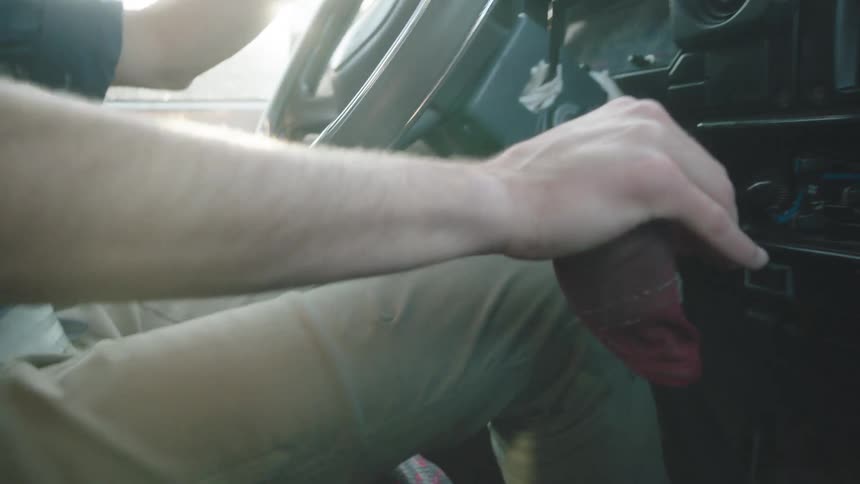 A man's hand rests on the gear shift of his vehicle as he drives on a sunny day with bright lens flare