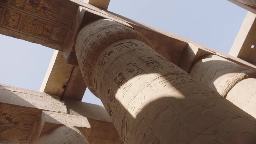 Sunlight illuminates the intricate hieroglyphic carvings on a colossal stone column inside an ancient Egyptian temple