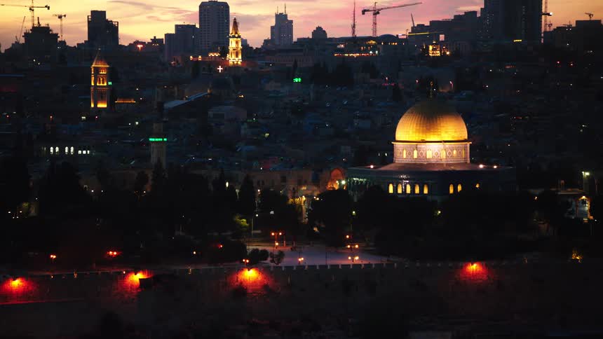 A stunning rack focus reveals the illuminated Dome of the Rock and the skyline of Jerusalem at sunset
