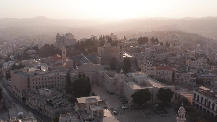An epic aerial view shows the Church of the Nativity and Manger Square in the historic city of Bethlehem during a hazy, golden sunrise